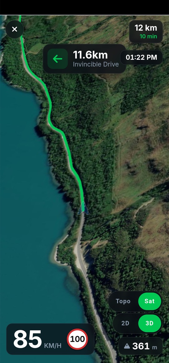 Turn-by-turn navigation on a phone in 3D satellite view, the route running along Lake Wakatipu, showing the next turn onto Invincible Drive in 11.6km, 12km and 10 minutes remaining, and 85 km/h against a 100 limit.